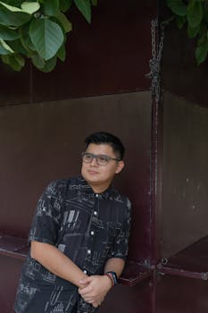 A relaxed man with glasses poses against a wall in an outdoor park in Merida, Yucatan.
