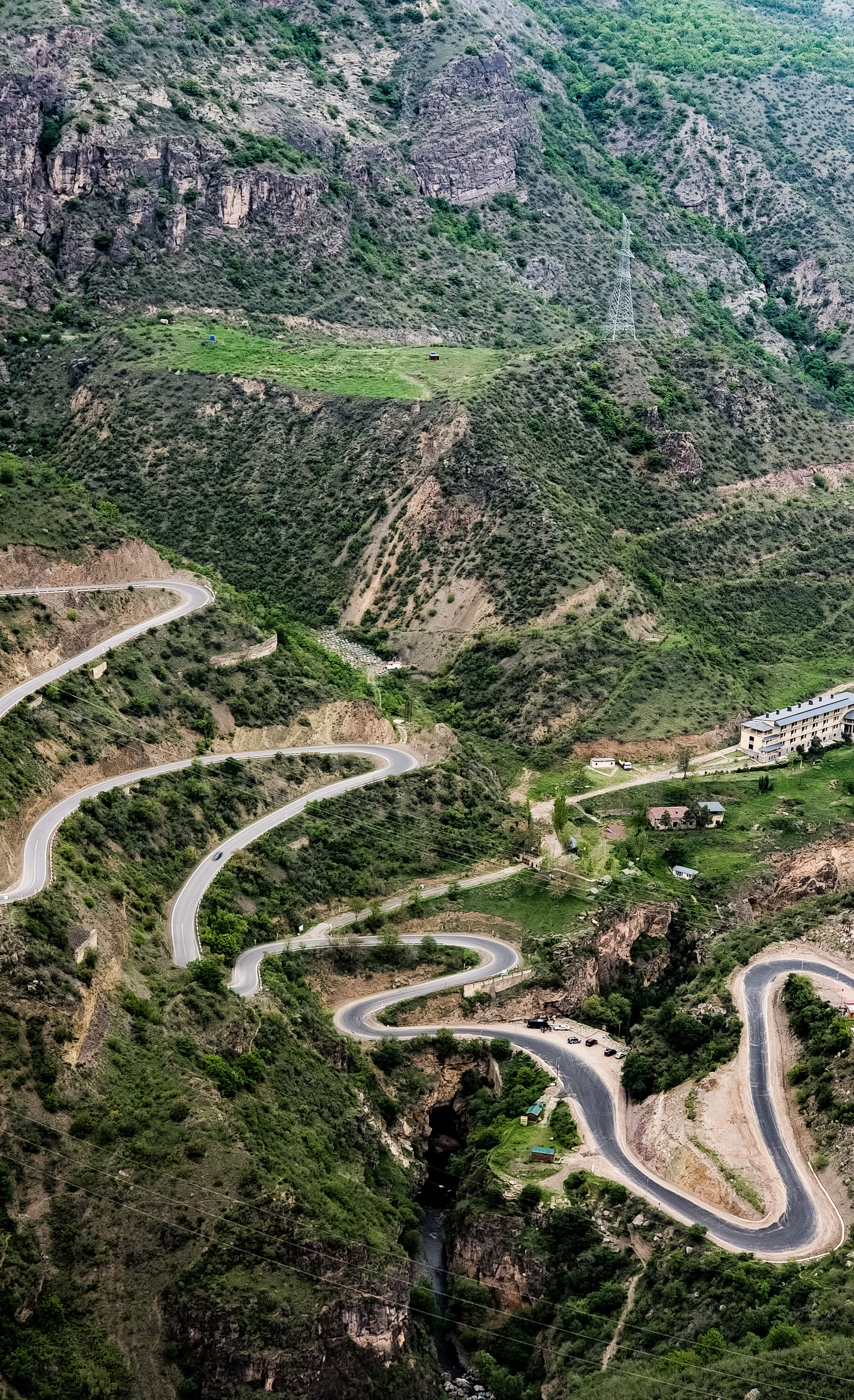 Aerial view of a winding mountain road in a green valley, showcasing nature's beauty.