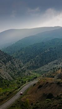 A winding road cutting through lush green mountains under a cloudy sky.