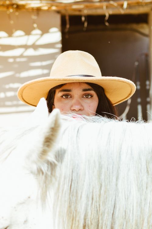 Free A woman in a wide-brimmed hat peers over a white horse outdoors. Stock Photo
