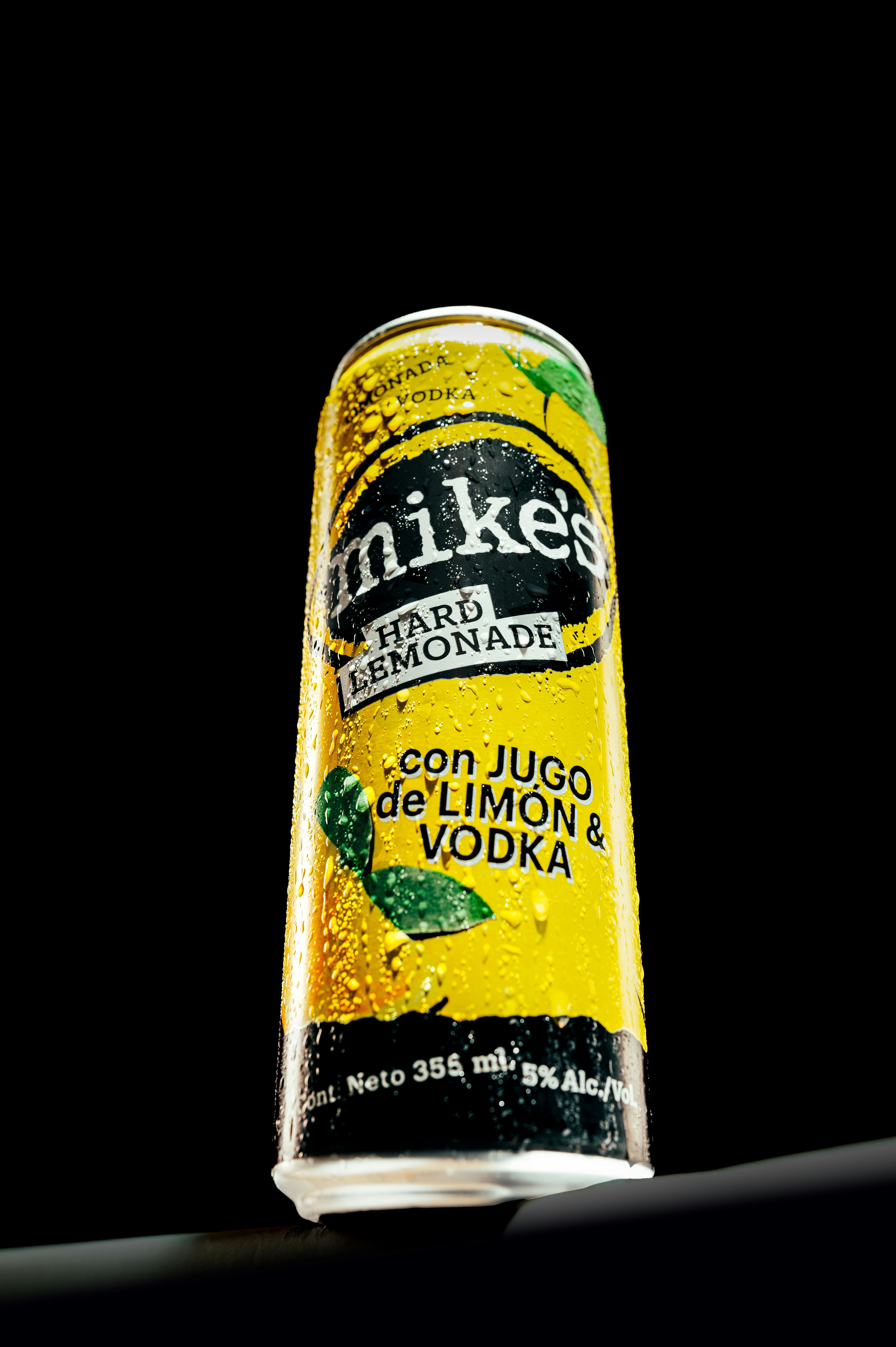 Close-up of a Mike's Hard Lemonade can with lemon and vodka on a black background.