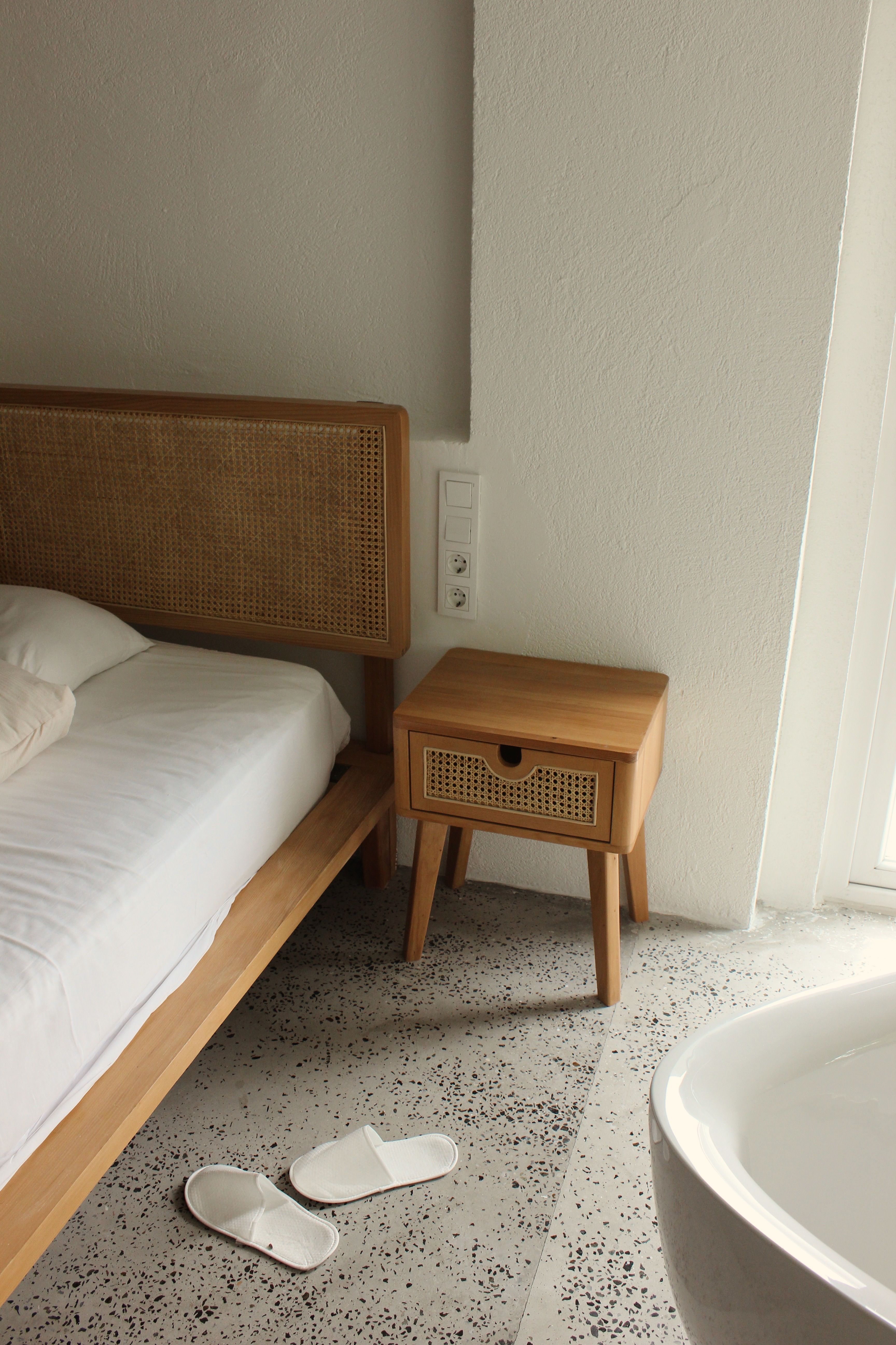 Small minimalist bedroom with pale walls, simple wood bed, matching stool and white bedding