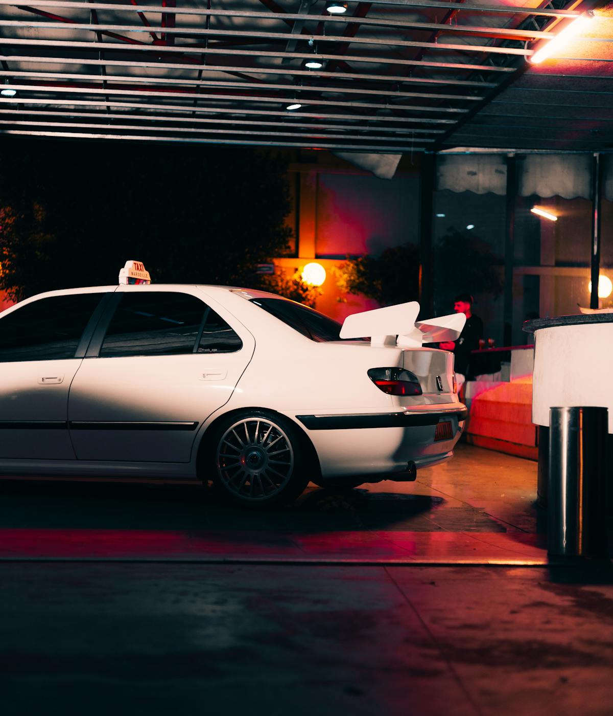 A white car parked in a dimly lit garage at night, with shadows cast on the walls.