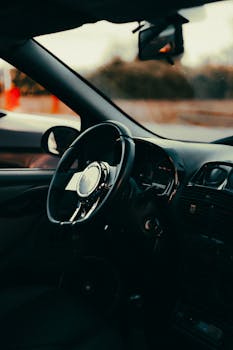 Car interior view focusing on steering wheel, showcasing moody lighting and reflective details.