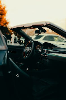 Interior of a luxury convertible car at sunset, showcasing the steering wheel and dashboard.