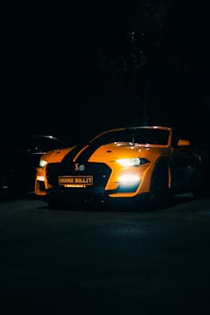 A striking orange sports car with black racing stripes glowing under streetlights at night.