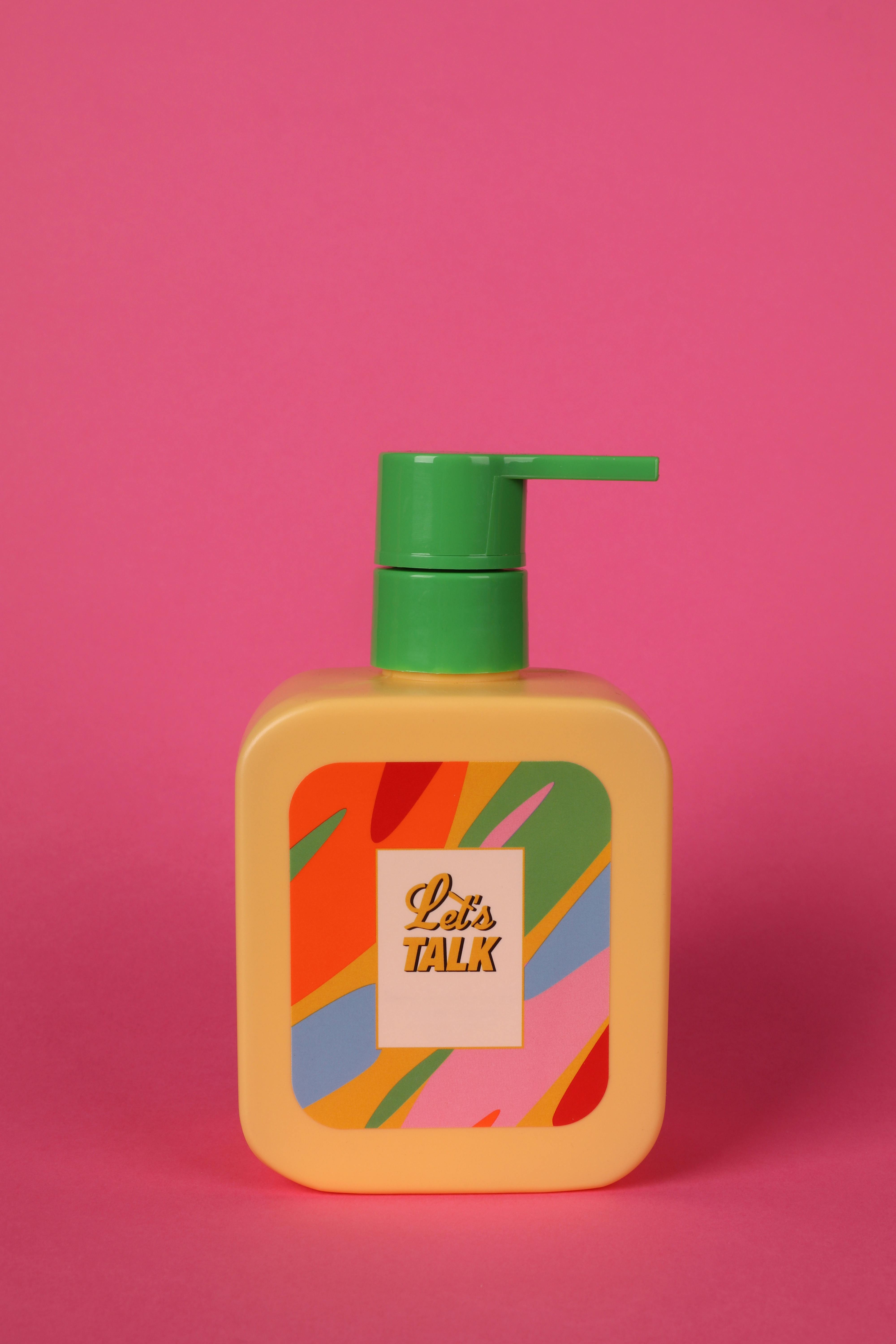 Vibrant soap dispenser with multicolored label against a pink background, promoting a lively vibe.