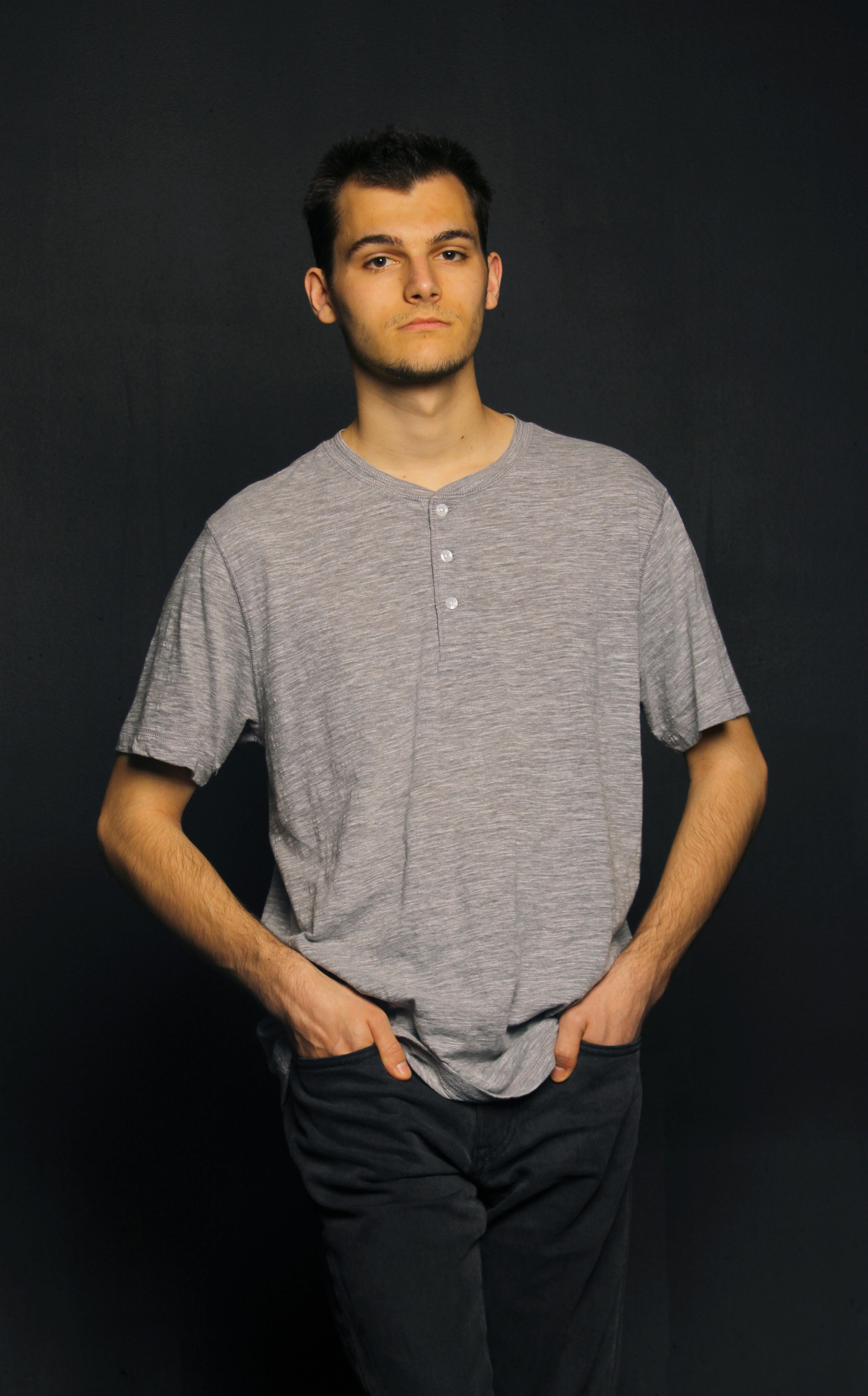 Miễn phí Chân dung một chàng trai trẻ mặc áo sơ mi xám giản dị, tay đút túi quần trên nền tối. Ảnh lưu trữ