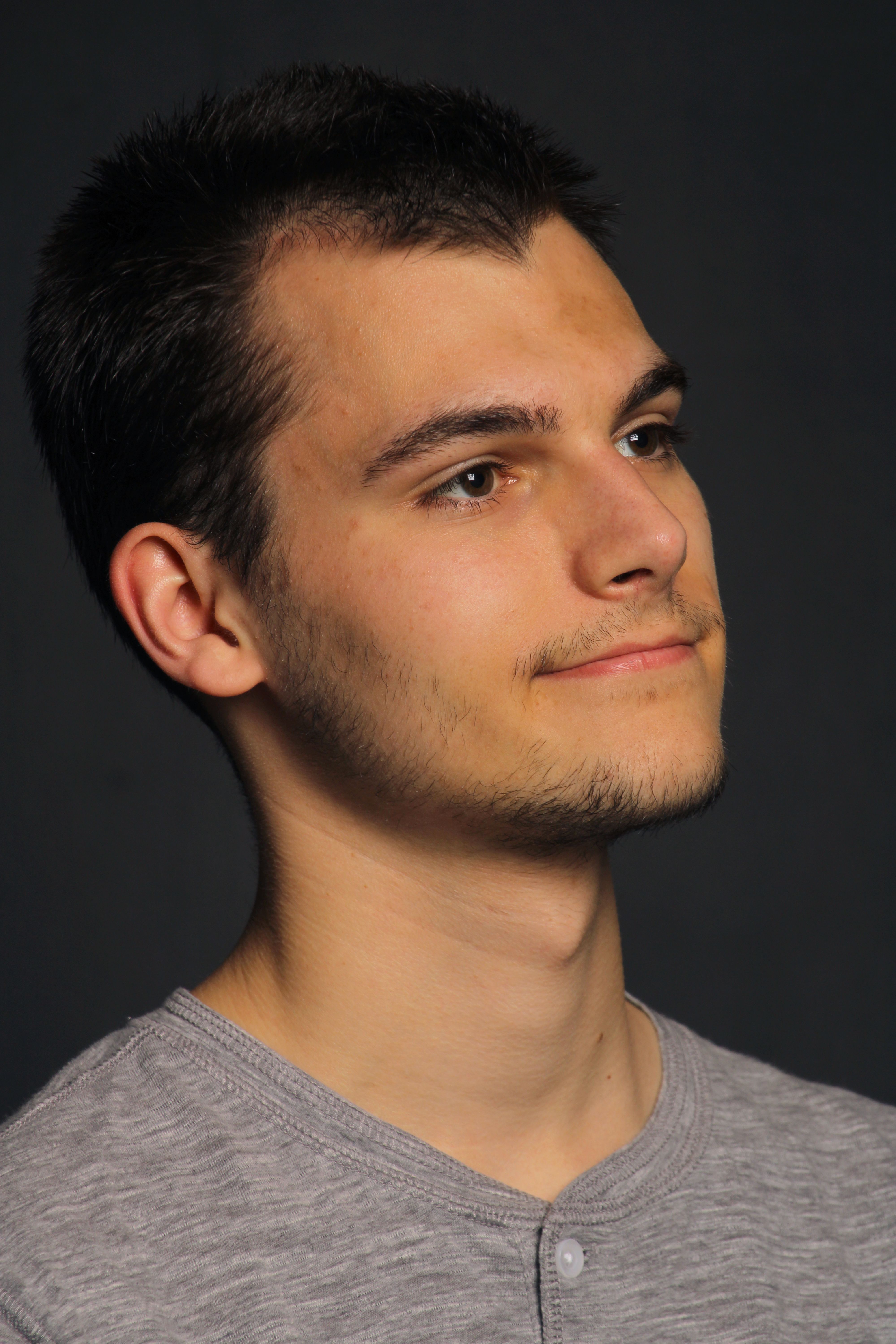 Portrait of a young man with a reflective expression against a dark background.