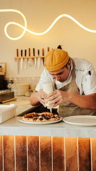 Chef decorating a gourmet pizza with sauce in a trendy kitchen setting.