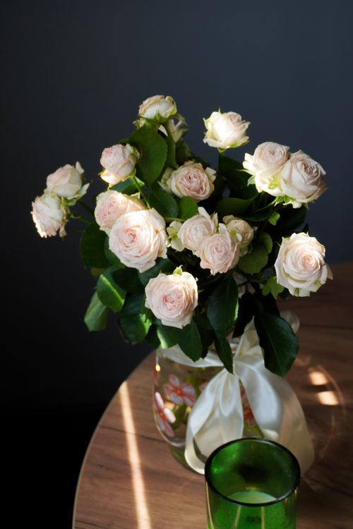Free A delicate arrangement of pink roses in a glass vase with soft sunlight highlighting their beauty. Stock Photo