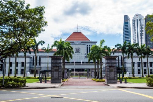 Free Exterior view of Singapore Parliament House with lush greenery and skyscrapers in the background. Stock Photo