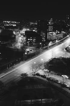 A long exposure capture of a city intersection at night in black and white, showcasing urban life.