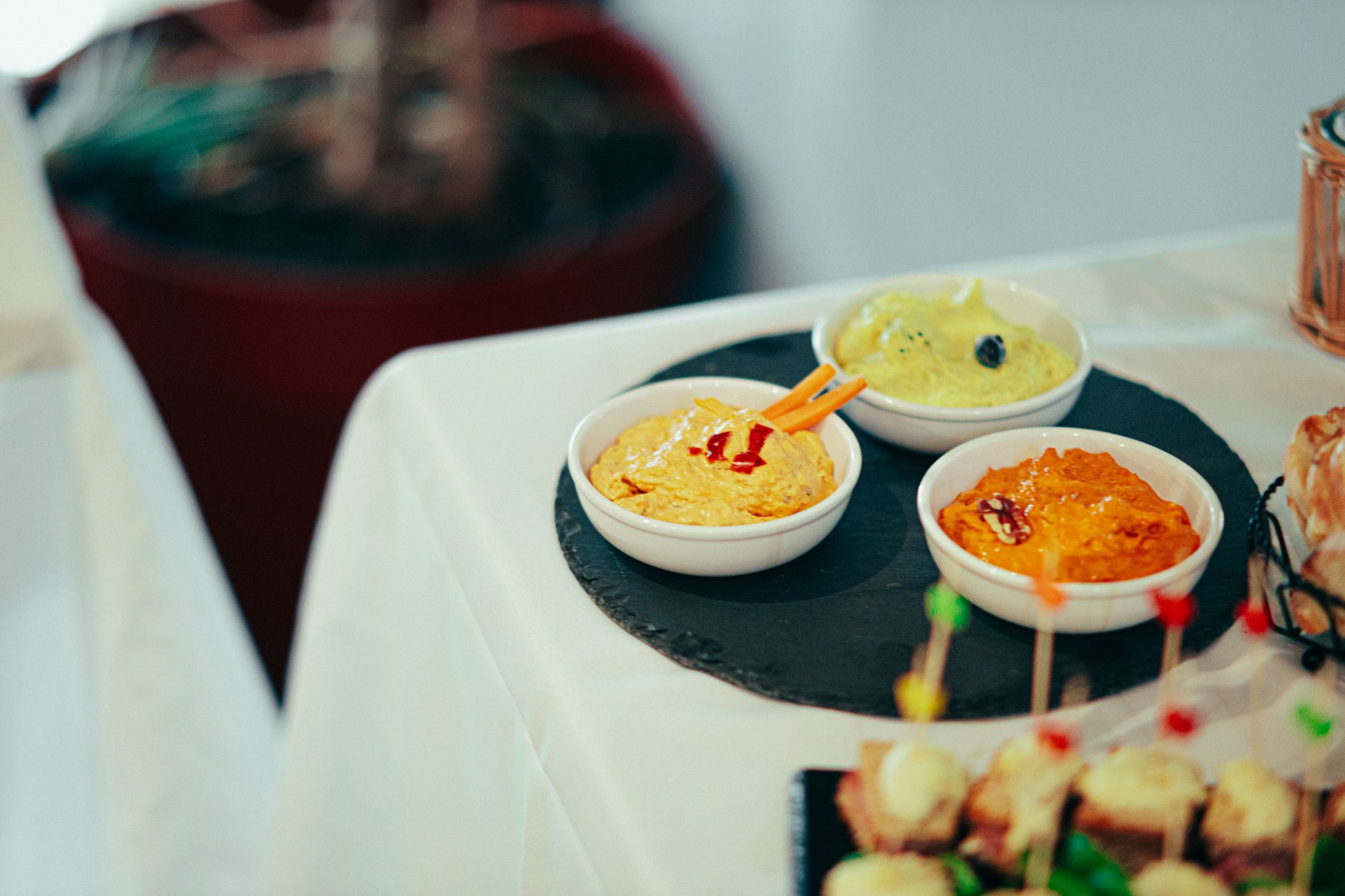A variety of colorful dips served in bowls on a slate platter at a buffet table.