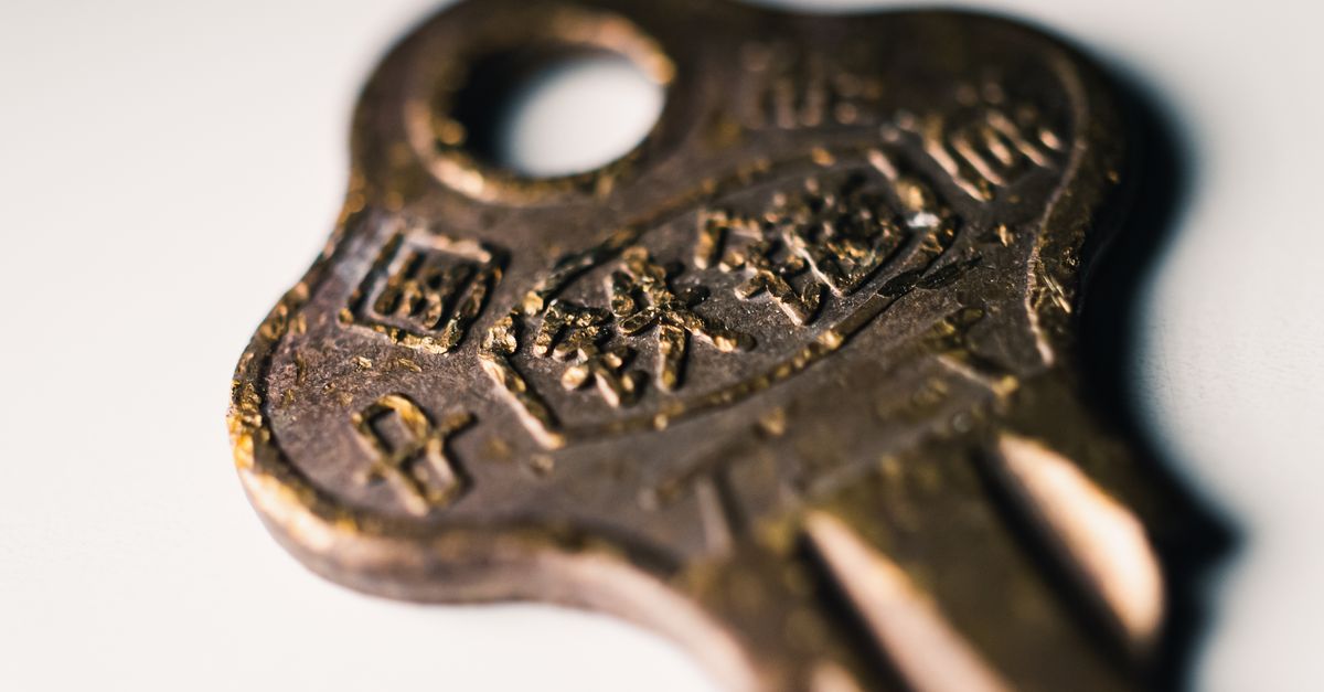 Macro shot of an old brass key featuring worn text on a white surface.