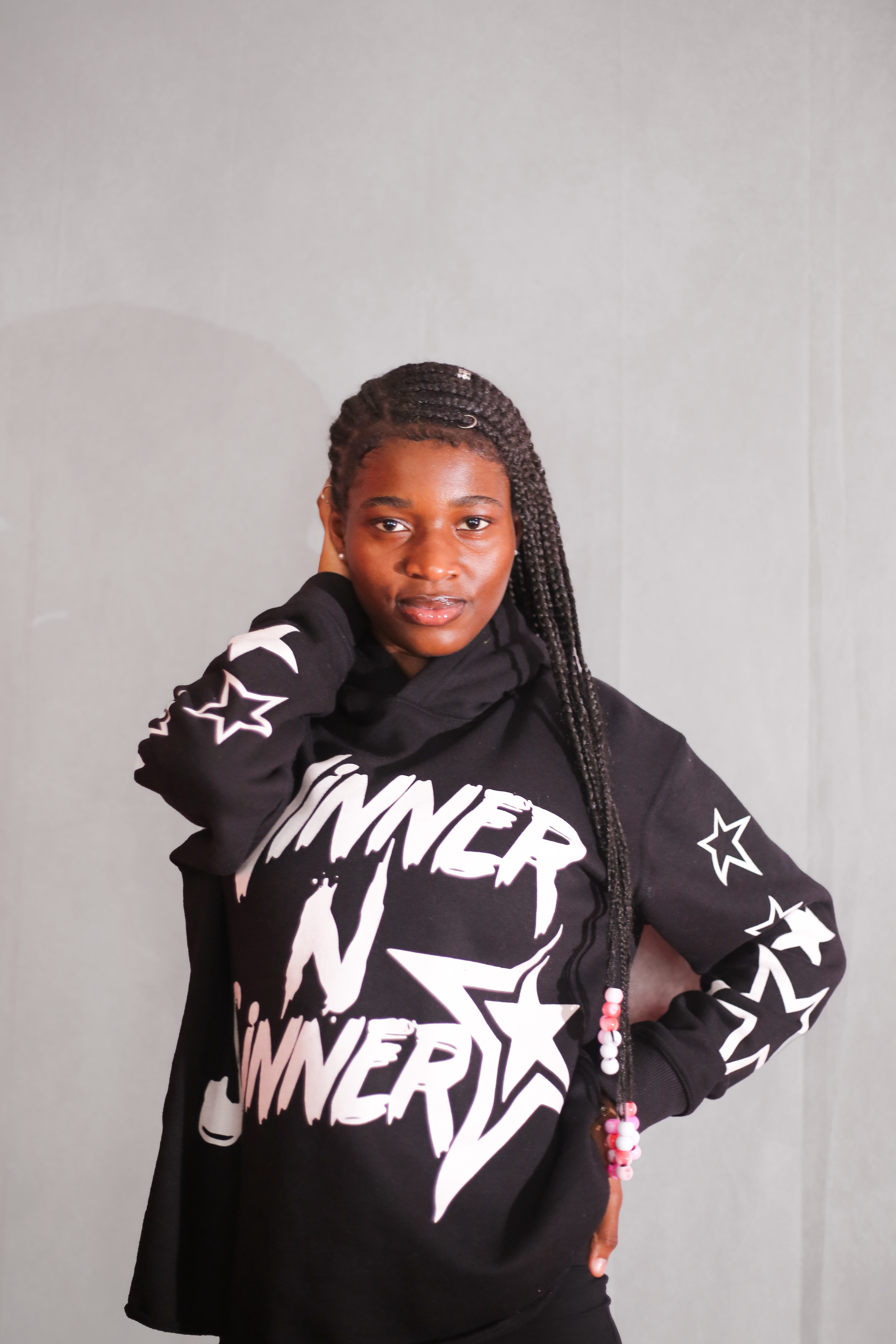 Portrait of a confident young woman posing in a graphic hoodie against a plain backdrop.