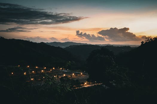 Serene twilight view of mountains with glowing lights and dramatic clouds.