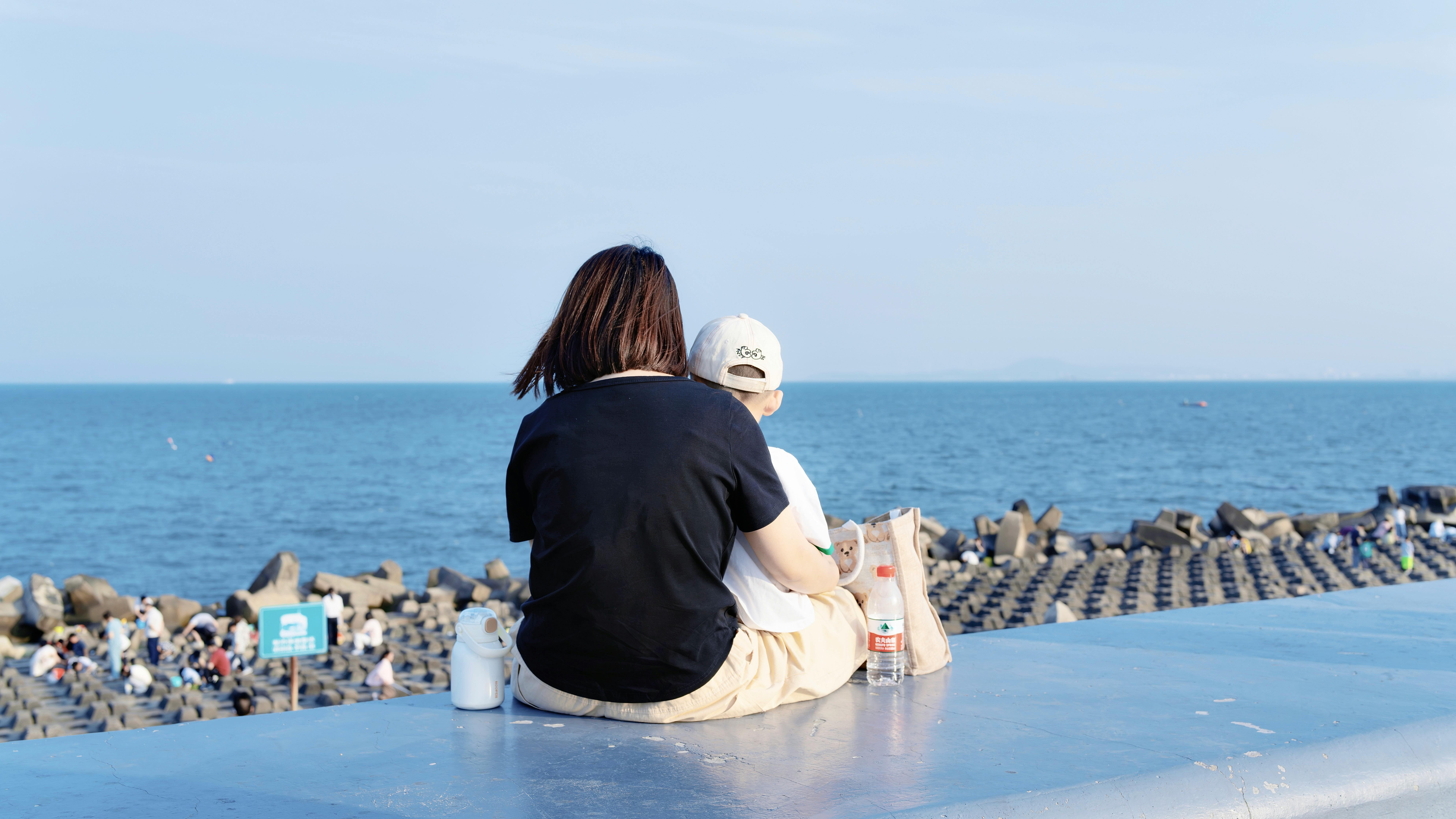 Mother and child sitting on seawall enjoying the ocean view.