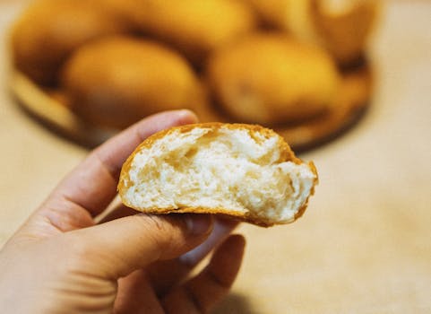 Close-up of a hand holding a piece of freshly baked Japanese bread indoors.