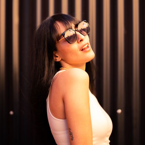 Free Confident woman in sunglasses with a tattoo poses stylishly outdoors against a dark background. Stock Photo