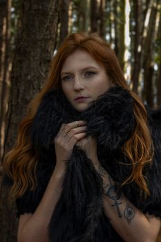 Moody portrait of a woman with red hair in a forest setting.