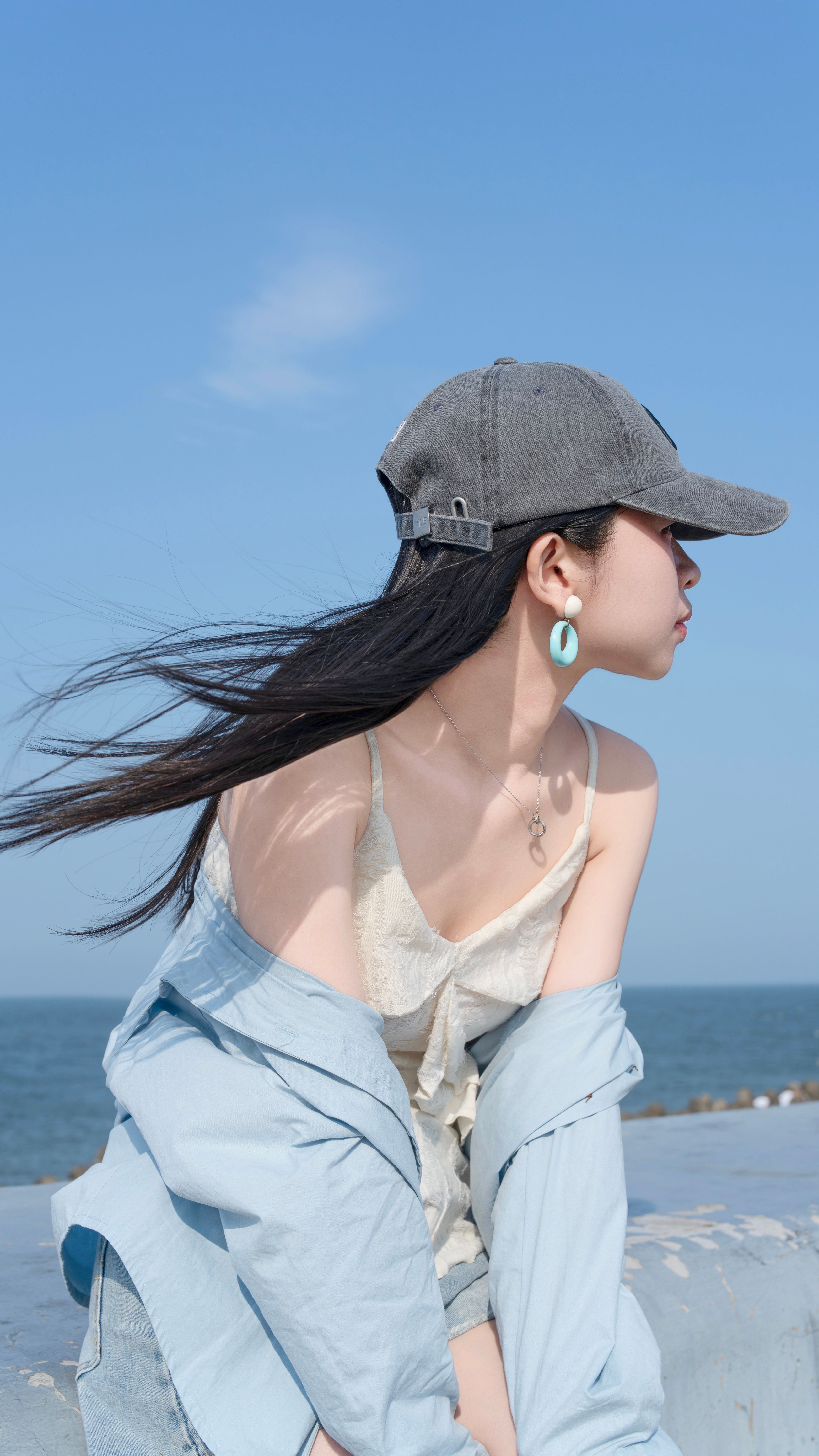 A fashionable woman enjoys a sunny day at the beach with the sea as a backdrop.