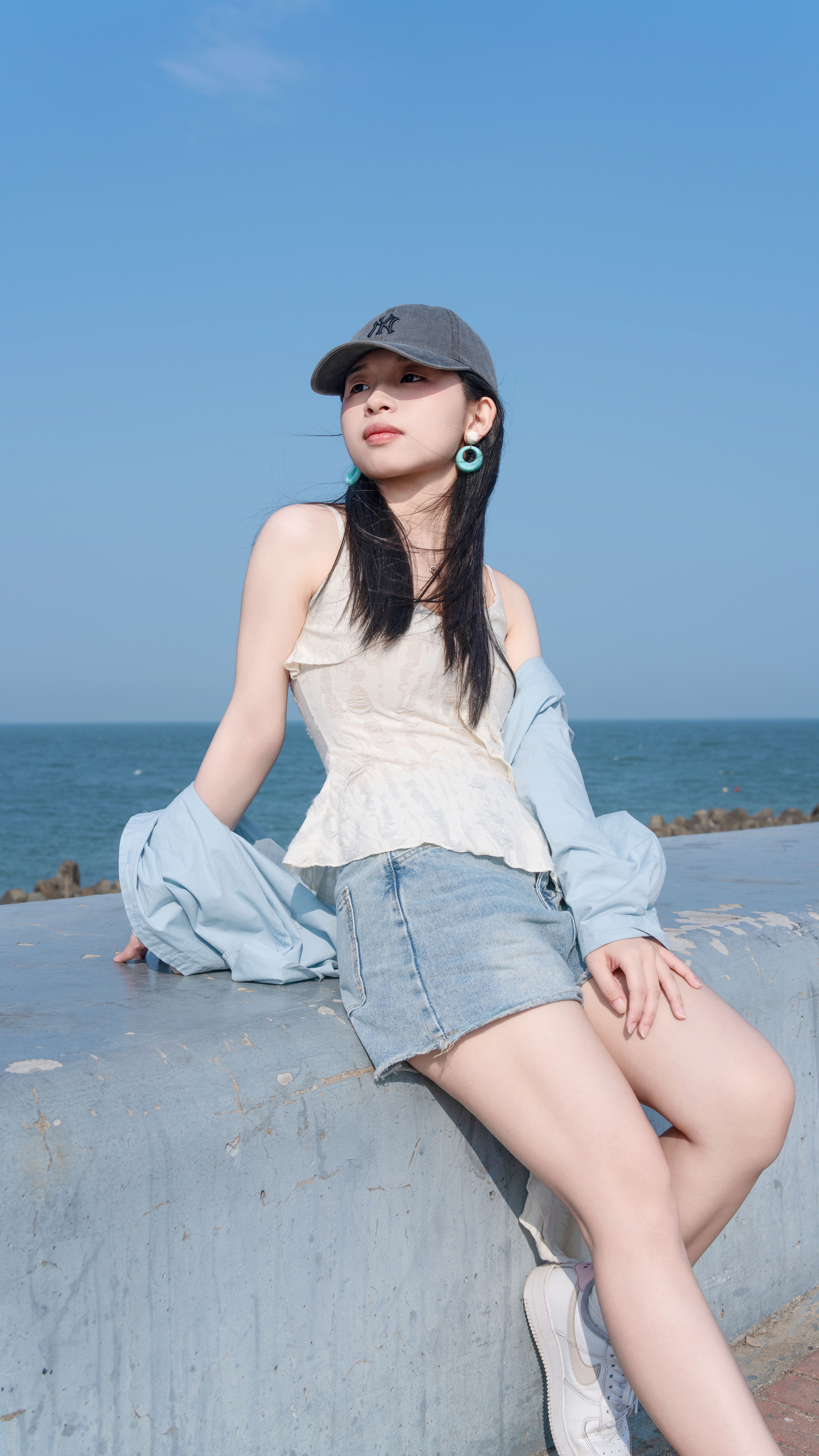 Stylish young woman in casual attire enjoying a sunny day by the sea.