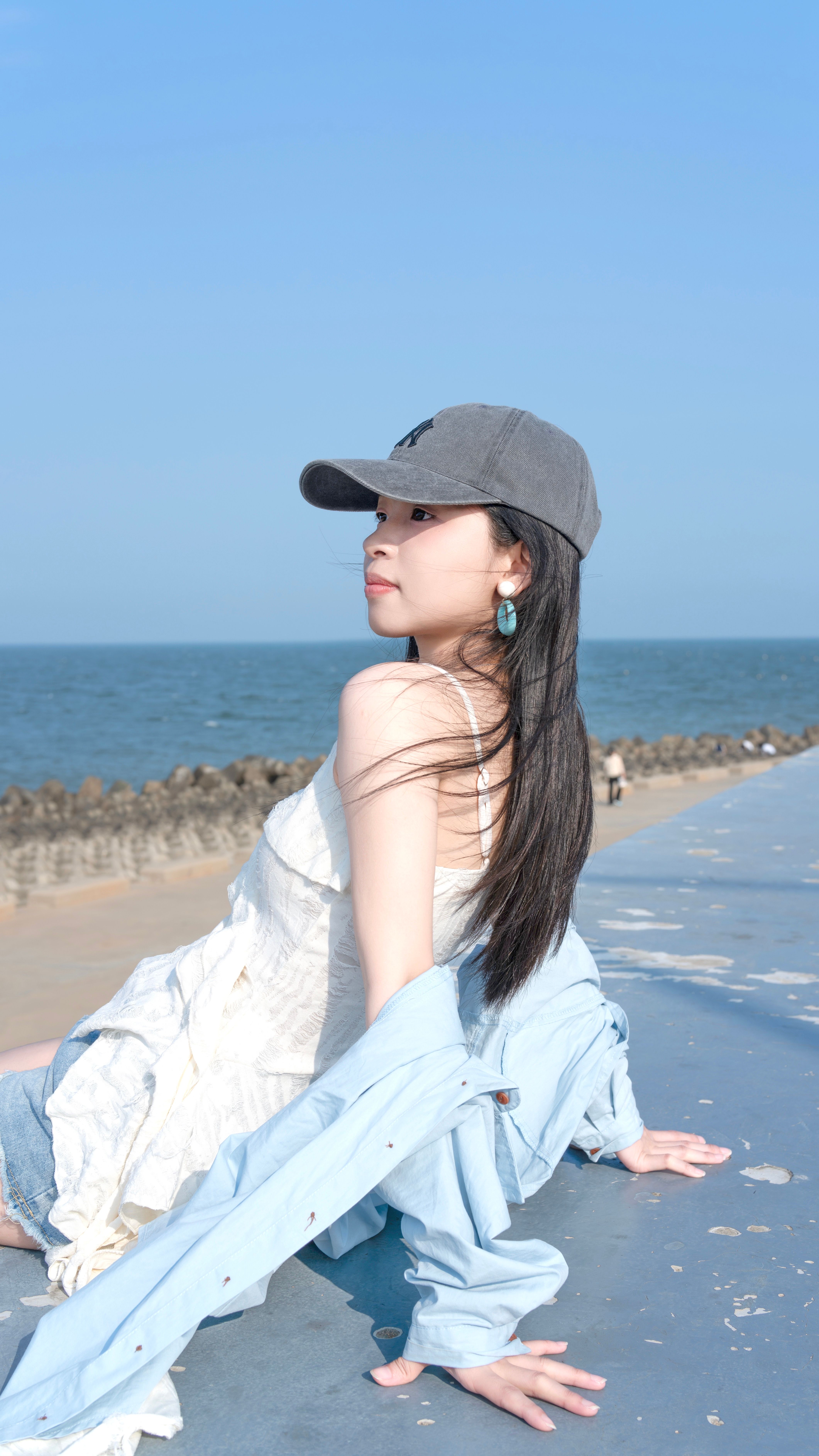 A young woman in casual summer attire sitting by the seaside, enjoying the sunny day.