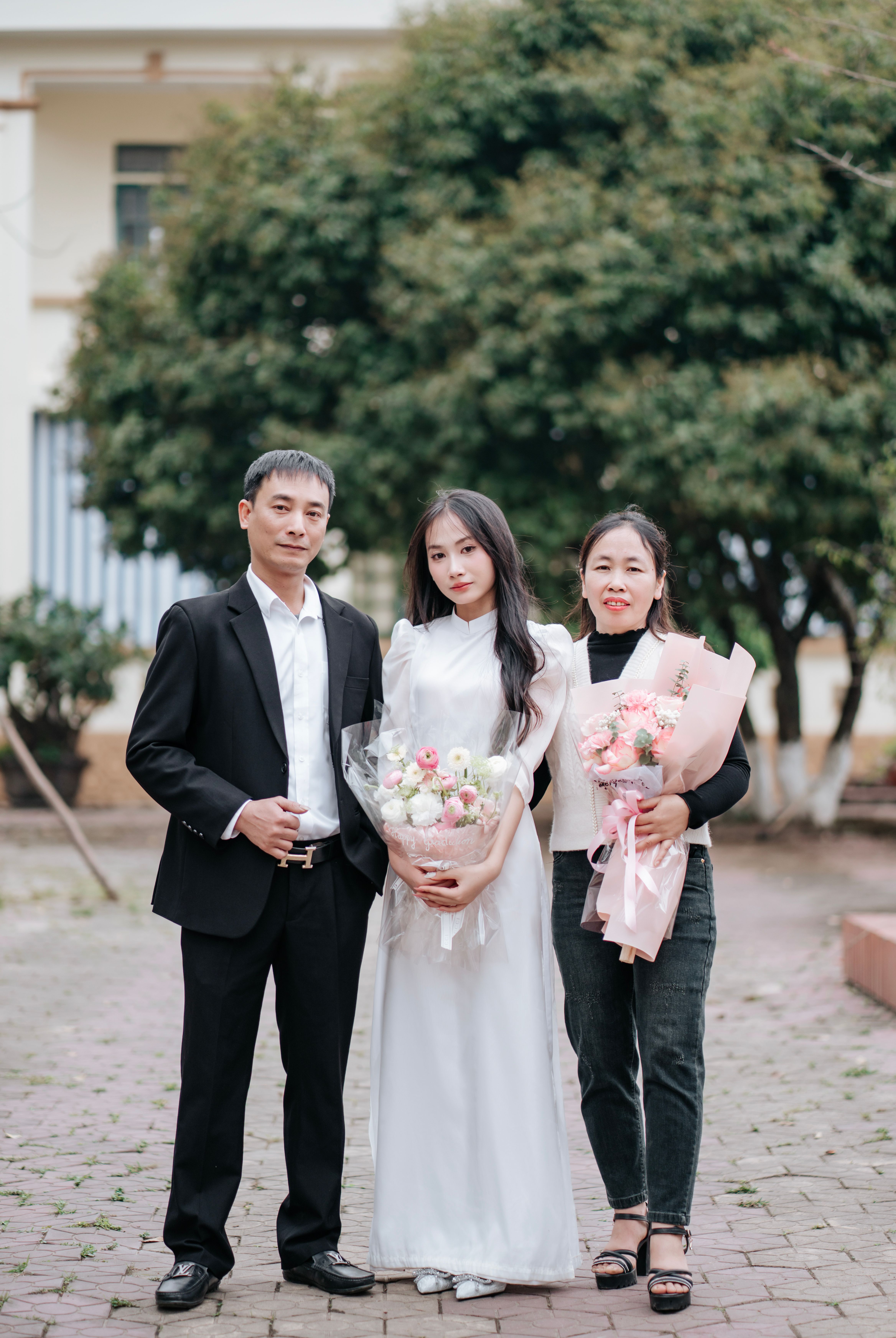 A family posing outdoors with flower bouquets, smiling together.