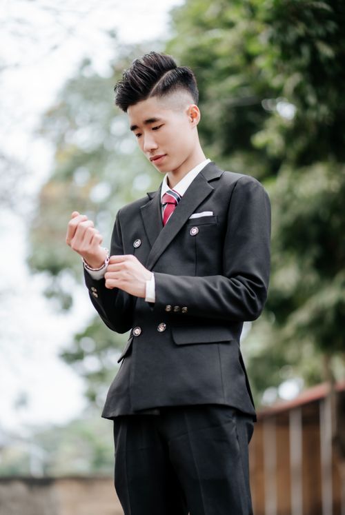 Free A young man in a stylish black suit adjusts his sleeve outdoors, exuding elegance and class. Stock Photo