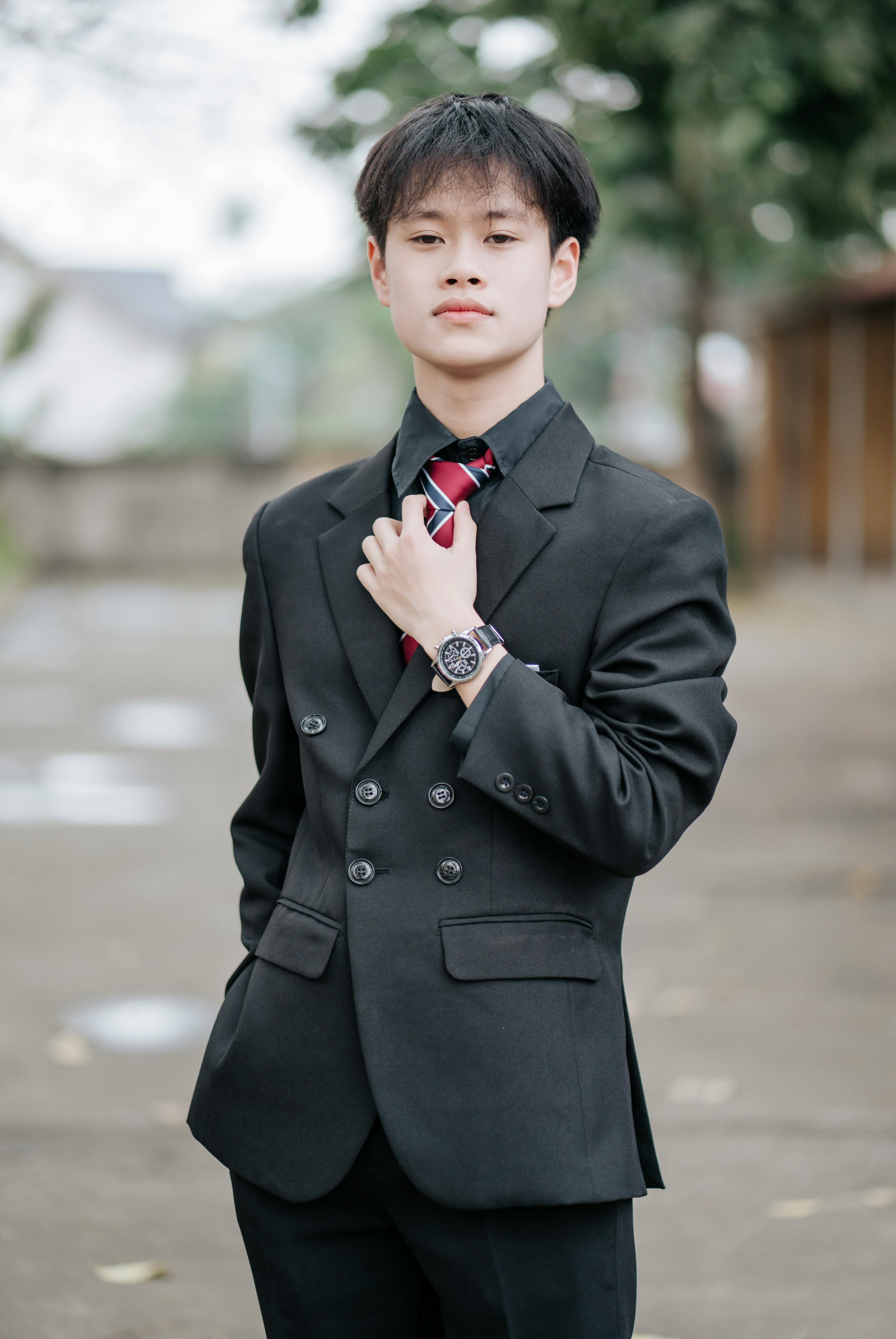 Confident young man posing in a black suit and tie outdoors.