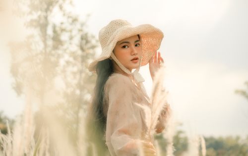 Free A stylish woman wearing a sun hat and white dress standing in nature with soft sunlight. Stock Photo