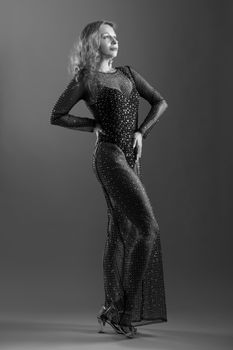 Black and white image of a woman in a sheer, beaded gown striking a confident pose.