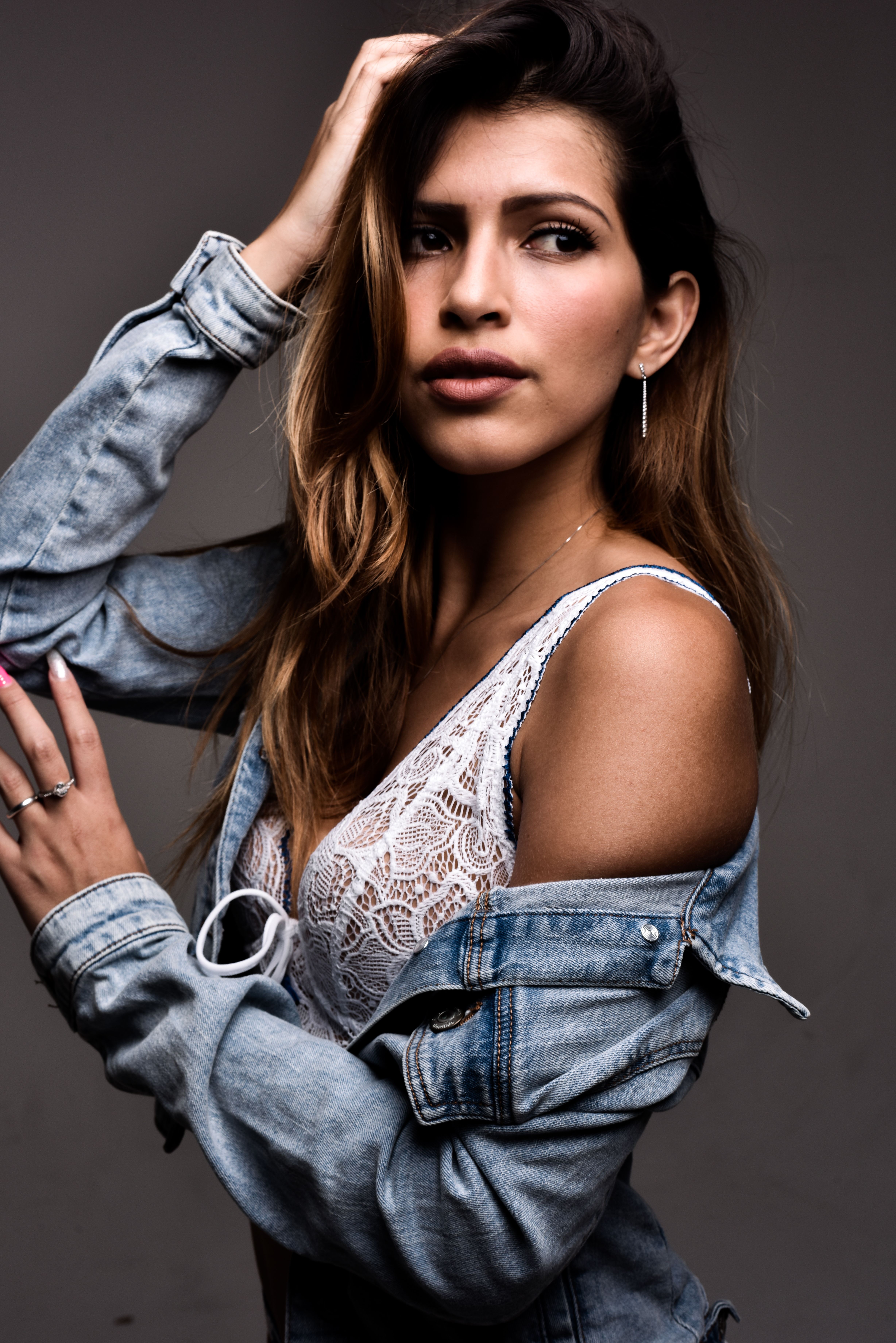 Stylish young woman in a lace top and denim jacket posing confidently indoors.