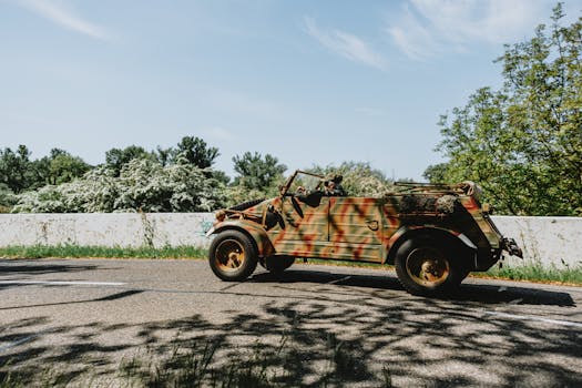Old military jeep with camouflage paint driving on a sunny outdoor road.