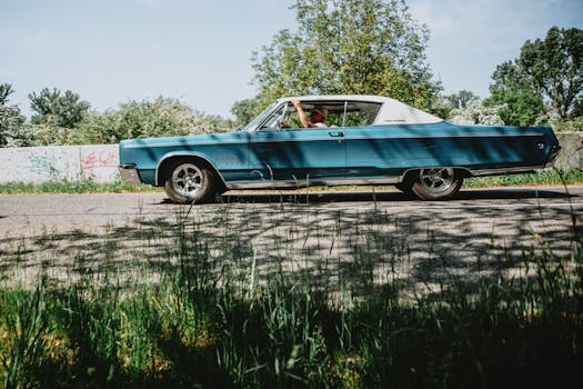 Classic blue car cruising on a scenic road on a sunny day, capturing a nostalgic vibe.