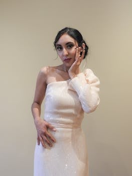 Young woman in an elegant, one-shoulder dress posing indoors with a soft background.