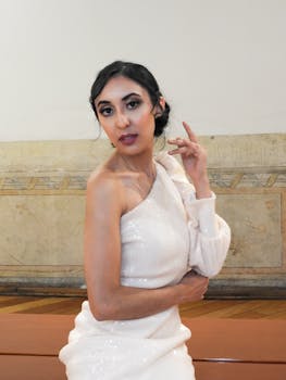 Elegant woman in white dress posing indoors with a confident style.