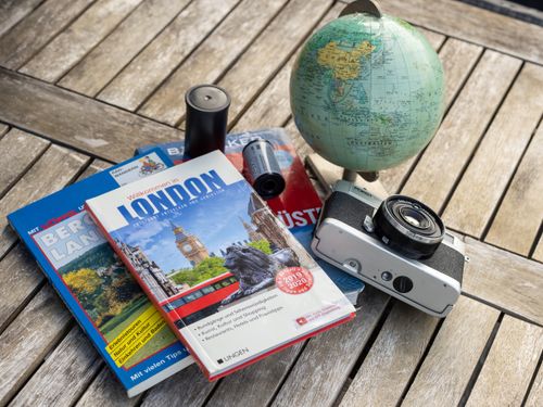 Free A vintage travel setup with guidebooks, a globe, and a film camera on a wooden table. Stock Photo