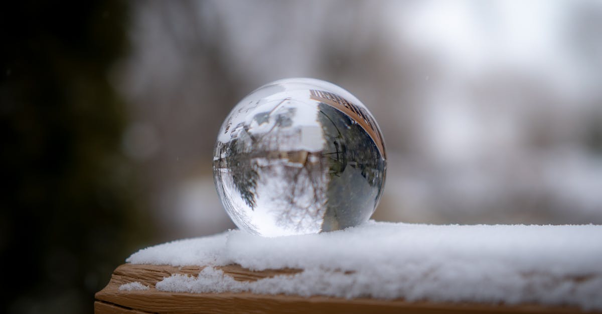 A crystal ball sitting on a snowy ledge reflecting a wintry landscape in soft focus.