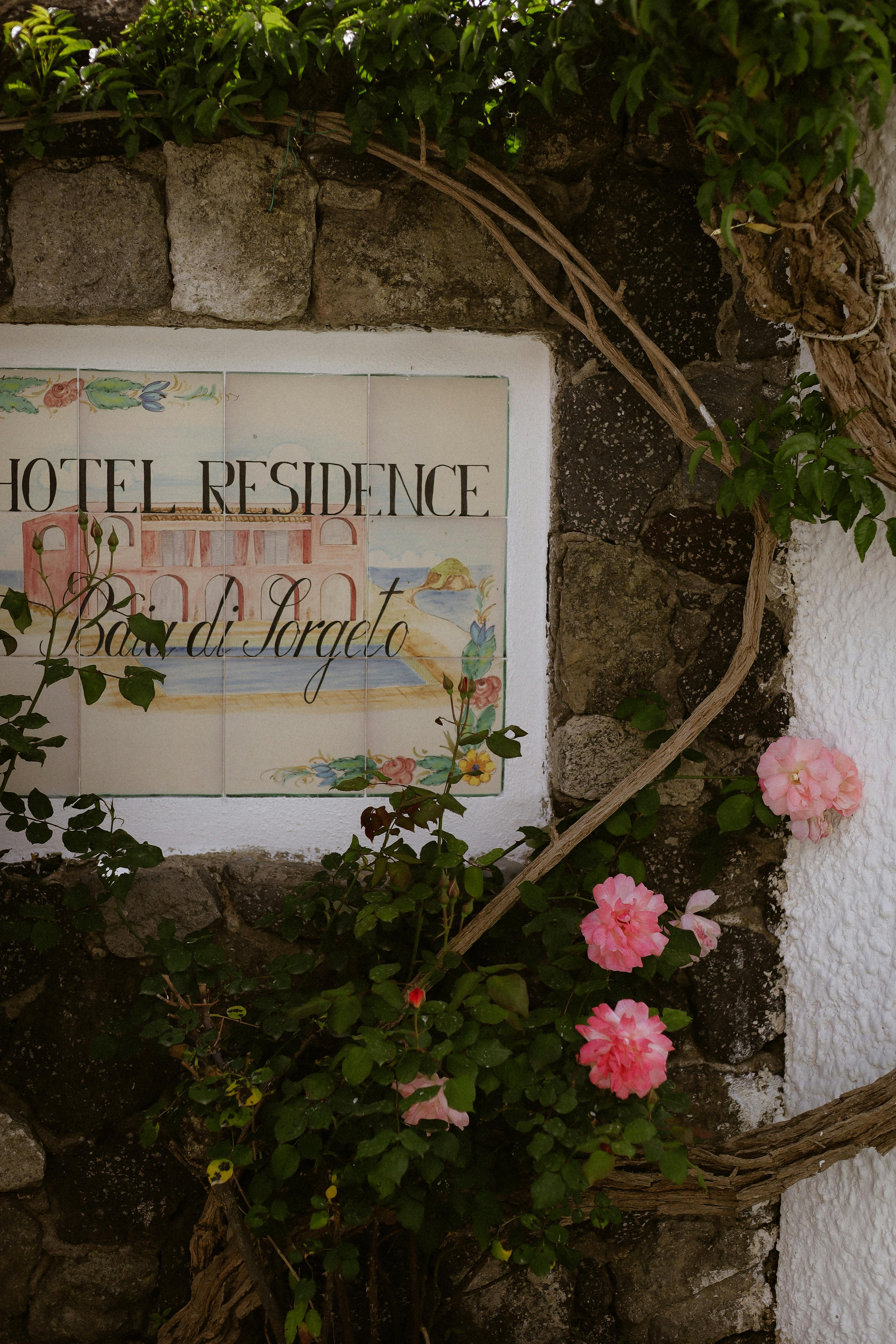 Charming stone wall with colorful flowers and a vintage hotel residence sign.
