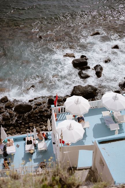 Aerial view of a sunny beachside terrace with umbrellas and people relaxing.