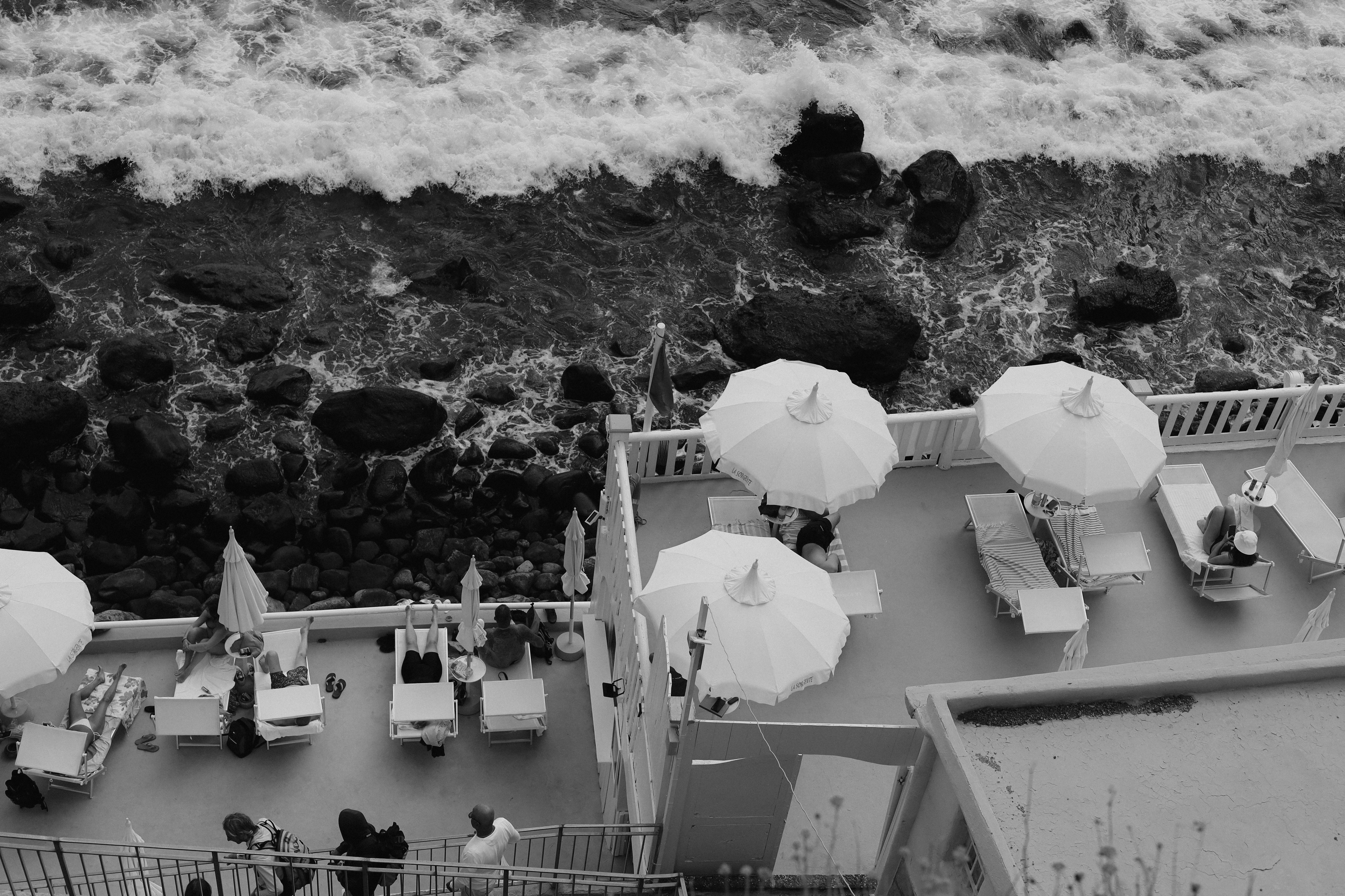 Aerial view of a seaside terrace with umbrellas and lounge chairs in monochrome.