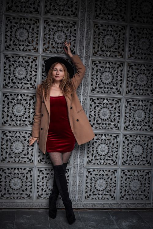 Free Fashionable woman in red dress and coat posing against an ornate patterned wall. Stock Photo