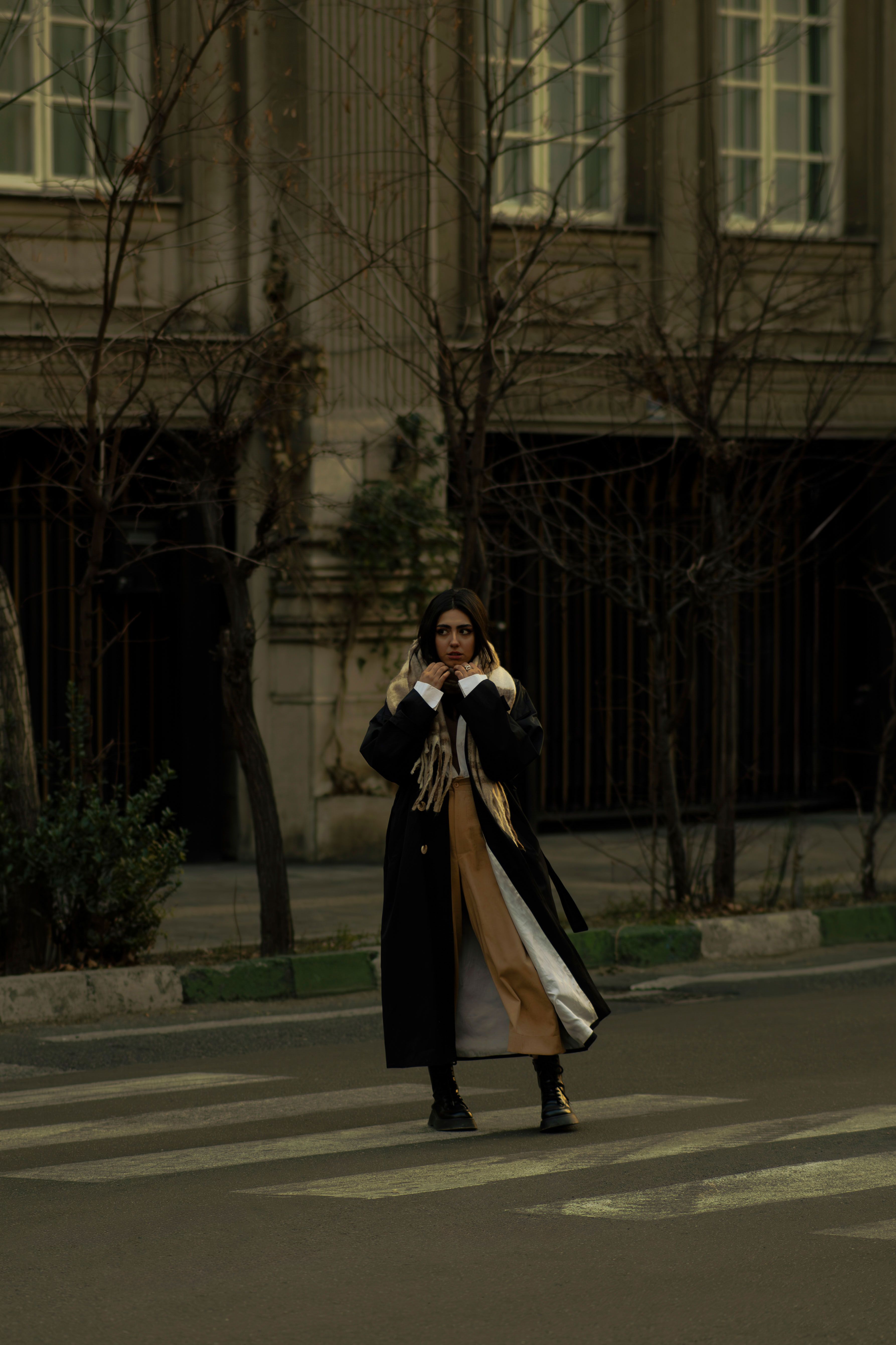 Stylish woman in winter attire standing on a crosswalk in Tehran, showcasing urban fashion.