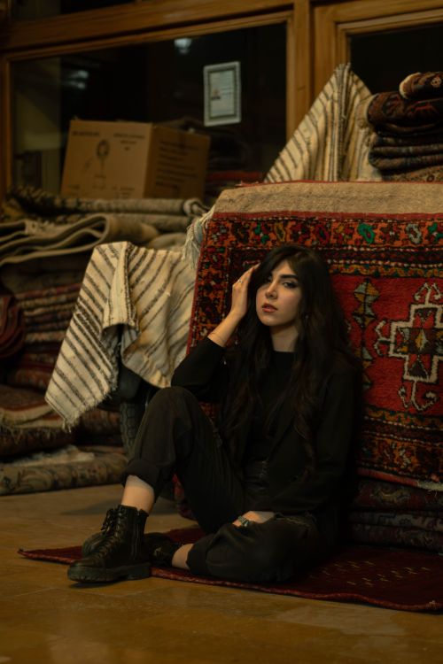 Free Fashionable woman sitting amidst colorful Persian rugs in Tehran shop. Stock Photo
