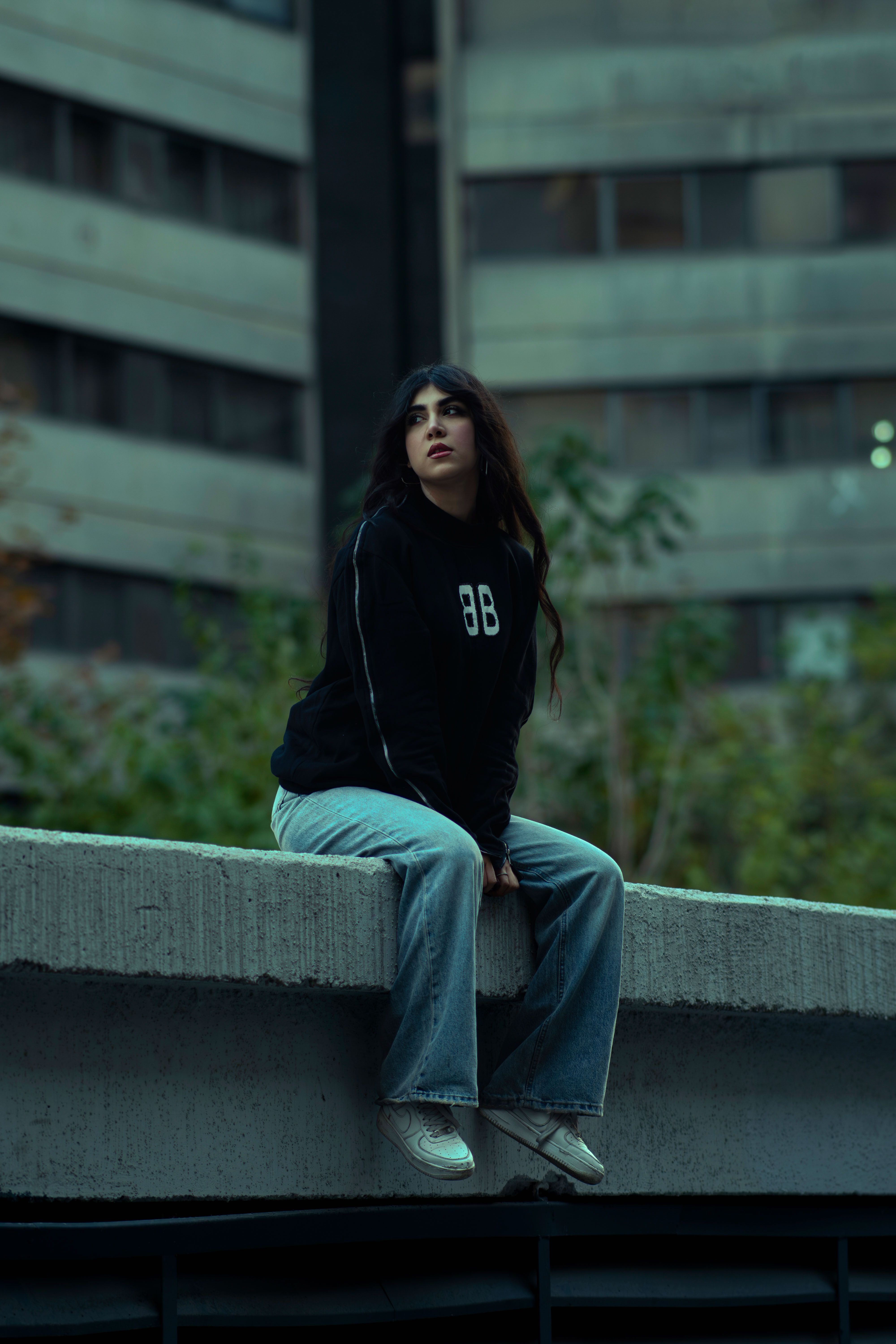 Stylish woman sitting on ledge amidst urban landscape in Tehran.