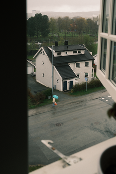 View of a person with an umbrella crossing the street on a rainy day from an open window.