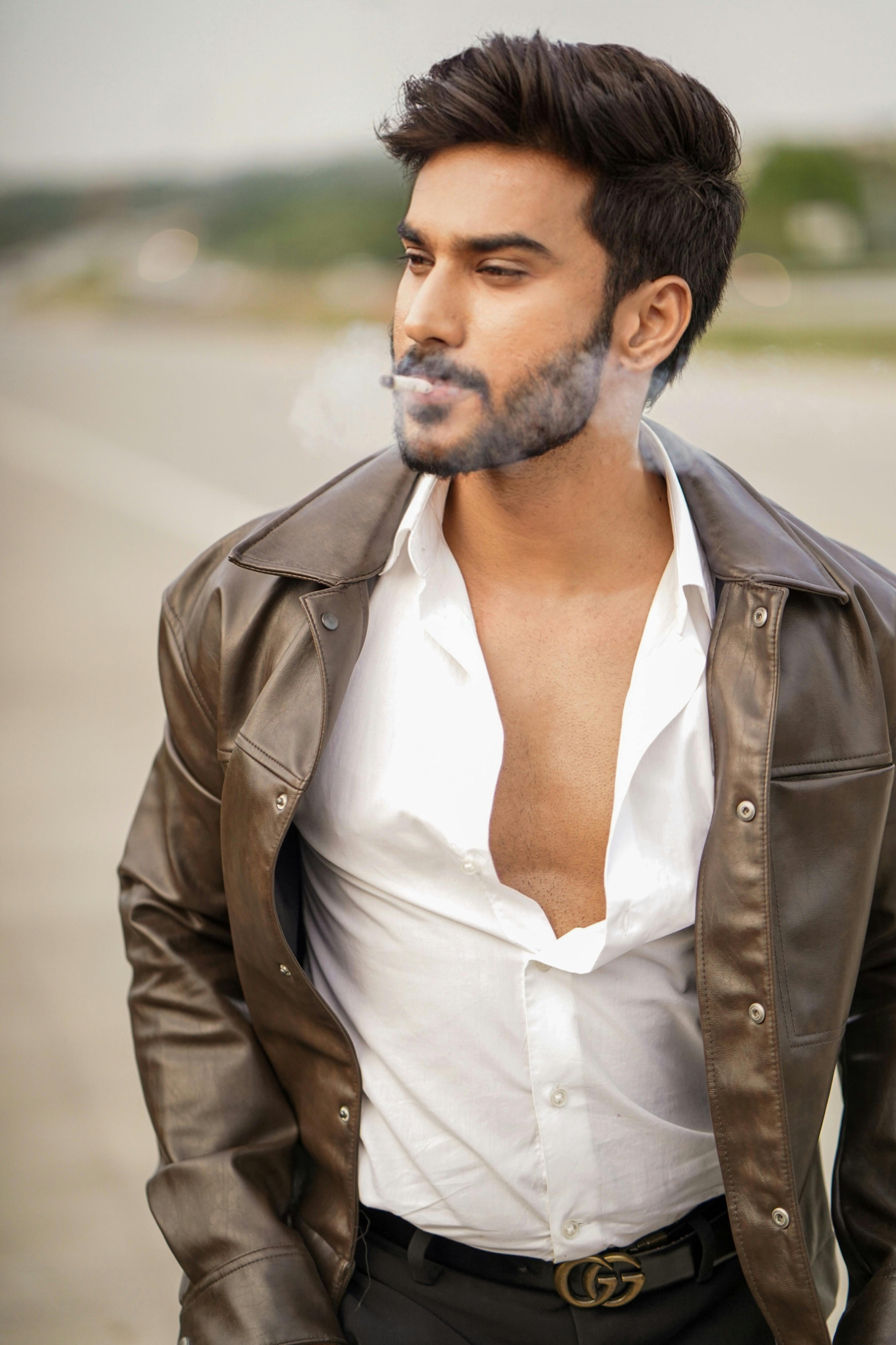 Young man with a trendy look smoking outdoors in a leather jacket.