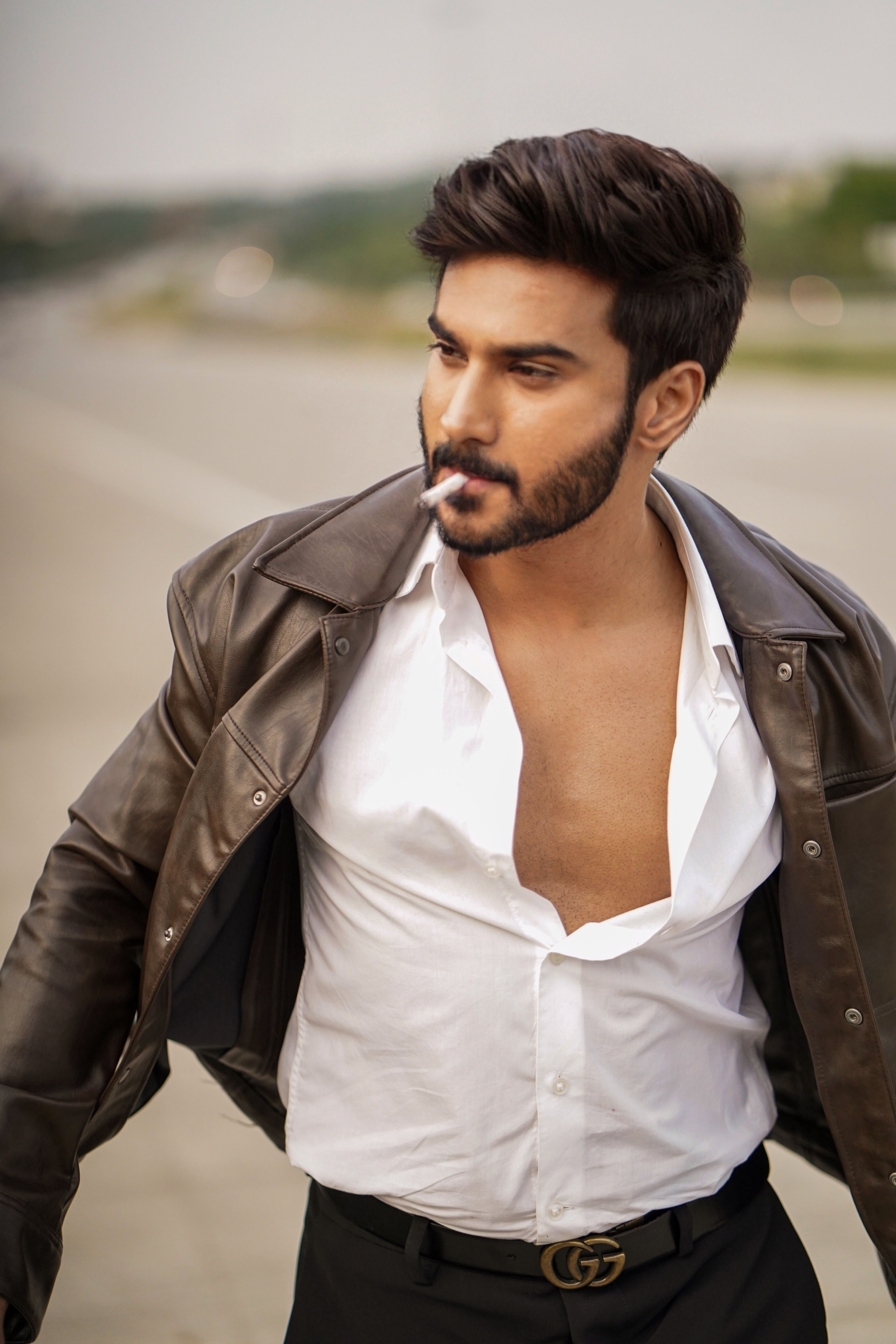 Confident man in leather jacket smoking cigarette on urban street.